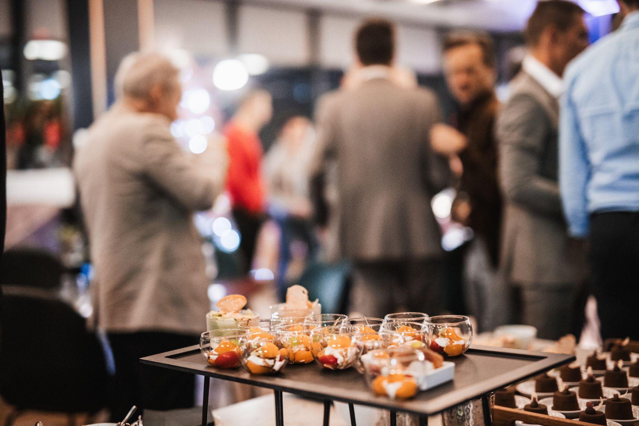 Glass dessert cups arranged on a table at a corporate cocktail reception, with business professionals socializing in the background.