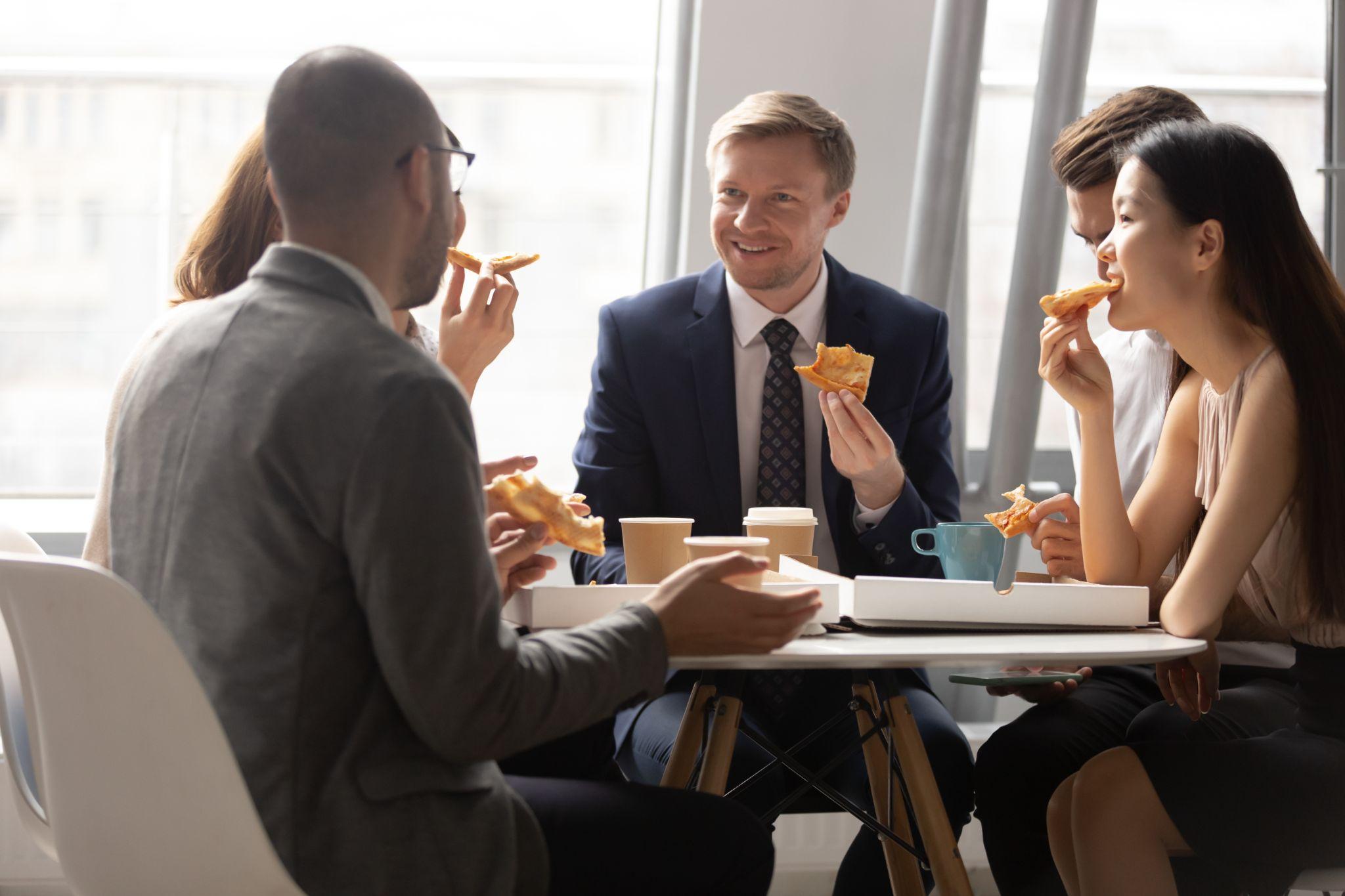 Office team sharing pizza during a lunch meeting, representing the connection and consistency achieved through multi-location office catering