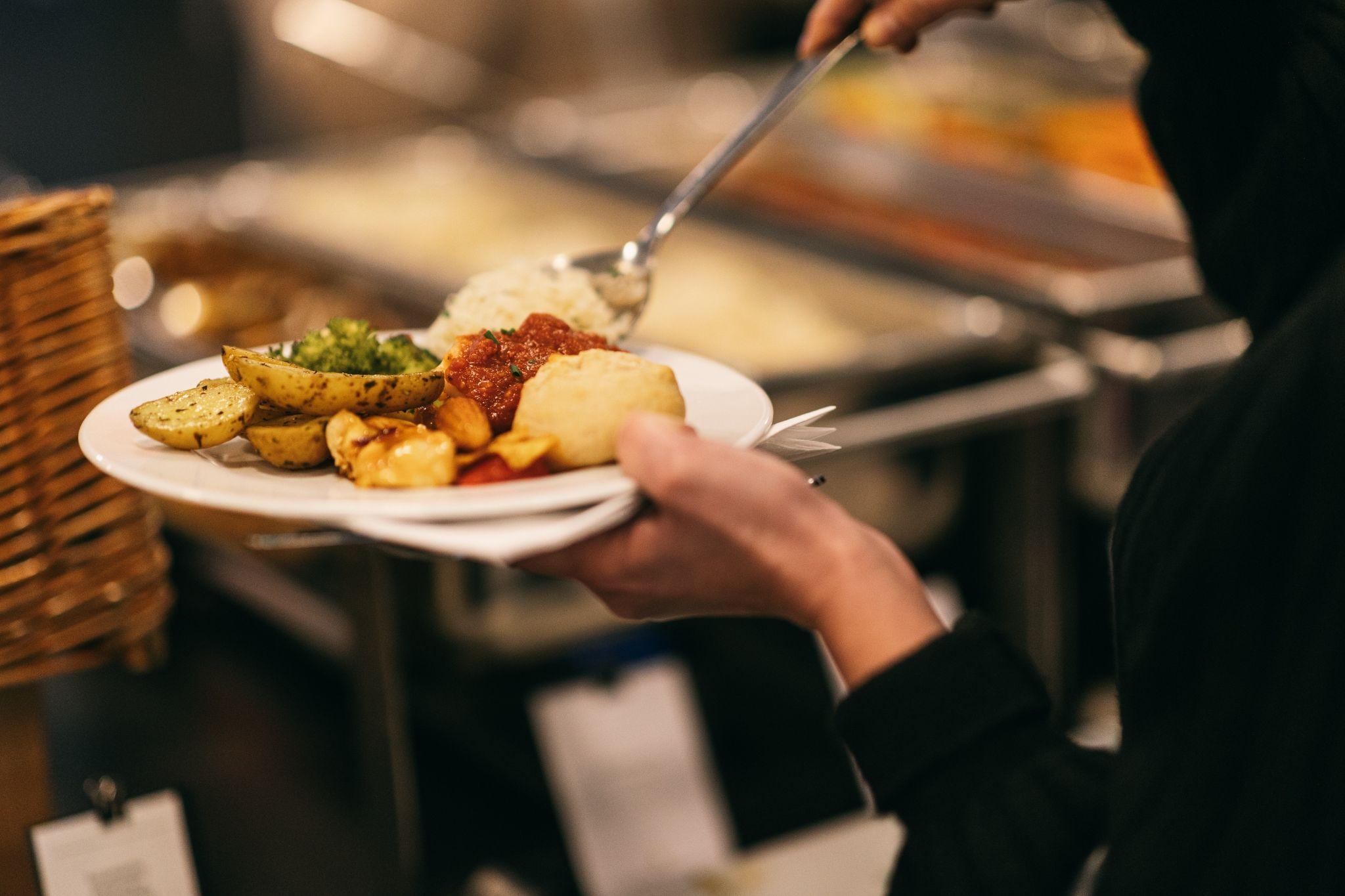 Employee serving lunch from buffet with vegetables and potatoes, showing balanced catering options for an engaging Lunch & Learn session