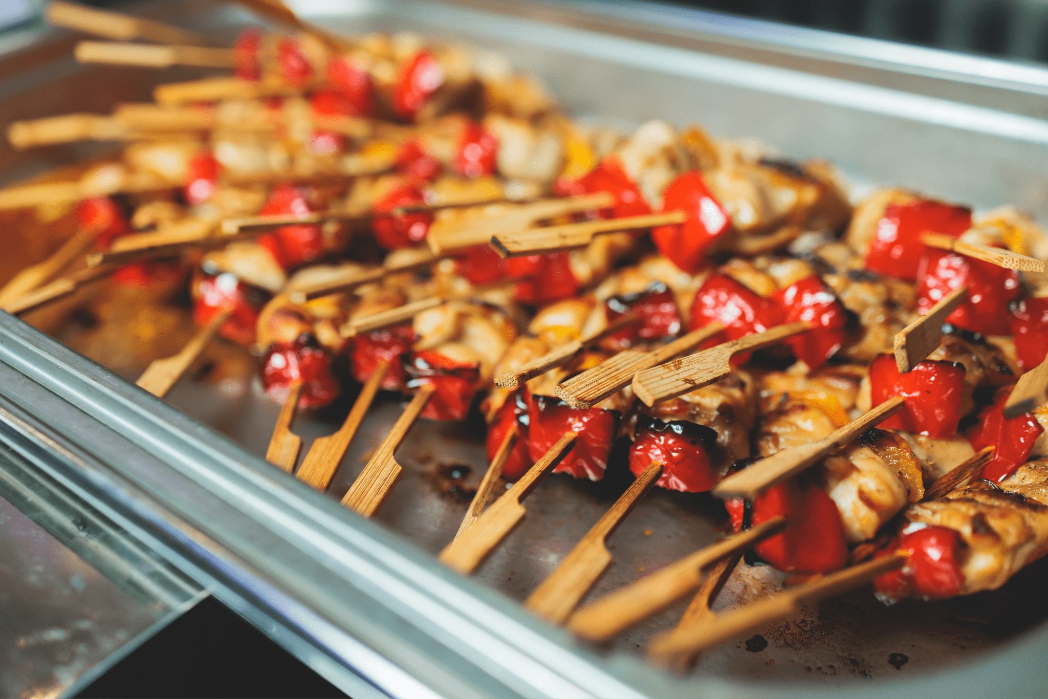 Grilled chicken and vegetable skewers displayed in a chafing dish, representing entrée options in tiered corporate catering packages.